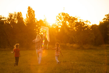 Naklejka na ściany i meble happy family mother and children run on meadow with a kite in the summer on the nature