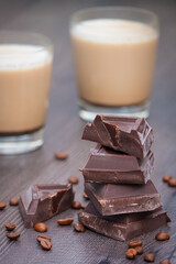 Pieces of dark chocolate, coffee beans and cups of cocoa or coffee with milk on wooden background.