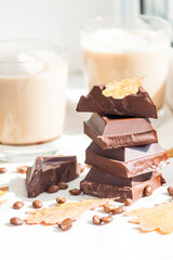 Pieces of dark chocolate, coffee beans and cups of cocoa or coffee with milk on white background. Autumn concept. Sunny day, yellow dry leaves.