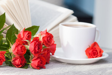 An open book with red orange roses and a cup of tea. Reading and relaxing. Romantic, sweet, dating concept.