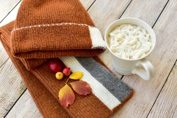 Cozy warm wooden toque and scarf with colourful fall leaves arranged in decorative autumnal background to represent autumn 