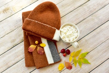 Cozy warm wooden toque and scarf with colourful fall leaves arranged in decorative autumnal background to represent autumn 