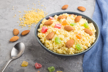 Millet porridge with candied fruits and almonds in blue ceramic bowl on a gray concrete background. Side view, close up.