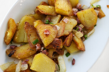 Crispy golden fried potatoes with onions and bacon served on a white plate, high angle view from above