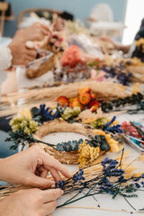 Girl making floral door wreath from colorful dry summer flowers and plants.  Fall flower decoration workshop