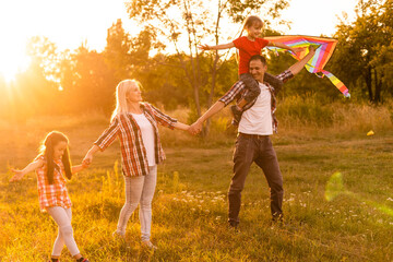 Happy family with a kite playing at sunset in the field