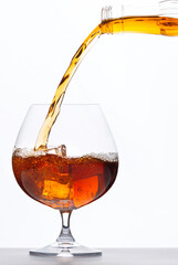Pouring whiskey drink into glass with ice cubes on white background
