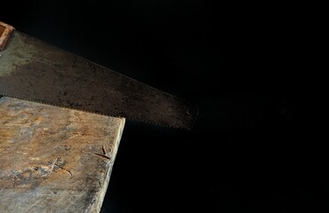 Old handsaw cutting a wooden board on black background. carpentry concept