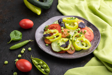 Vegetarian salad from green pea, tomatoes, pepper and basil on a black concrete background. Side view.