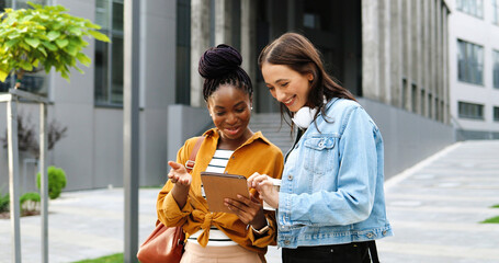 Mixed-races females talking and watching something on tablet device at street in city. Beautiful...