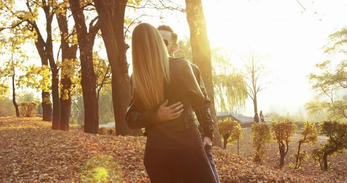 Happy couple in love stands in embraces and kisses autumn park with sun beams