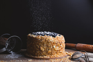 Napoleon cake with the blueberries sprinkled with powdered sugar next to the kitchen utensils on...
