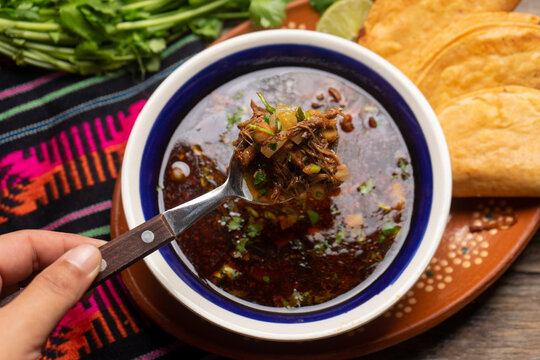 Mexican birria consome soup and tacos on wooden background