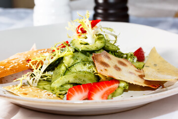 Salad with avocado, strawberries, frieze salad and chips is on the plate