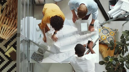 Top down shot of group of multiethnic male and female architects unrolling paper on office table, discussing construction plan and putting marks while working in team on project - Powered by Adobe