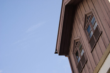 Fototapeta na wymiar Topo de uma casa construído em madeira com duas janelas e o céu a fazer fundo, formas triangulares cores azuis e castanhas