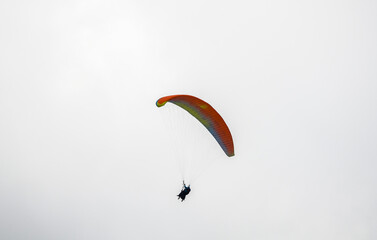 Paraglider silhouette flying in foggy sky in Carpathian mountains. Popular tourist extreme sport activity