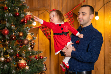 Proud dad decorates the Christmas tree while holding his little daughter in his arms. Family holidays, Christmas tale. Best childhood memories