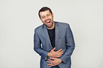 Young businessman man with a beard in a jacket smiling and laughing out loud because a funny crazy joke with hands on the body. Portrait of a man on a gray background