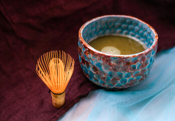 Bamboo whisk and a ceramic blue and brown bowl with Japanese matcha green tea brewed in it