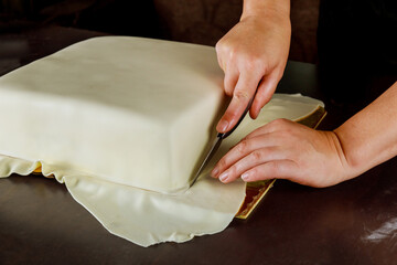 Woman cutting white fondant on square cake.