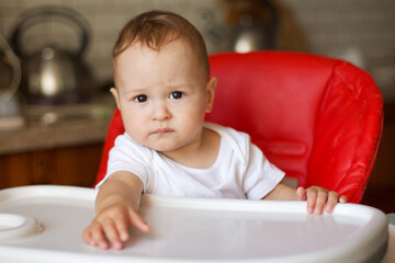Adorable cute baby boy with a serious look sits in the highchair, close-up portrait.
