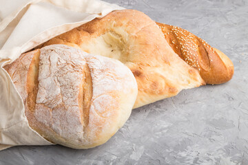 Reusable grocery bag with fresh baked bread on a gray concrete background. side view, copy space.