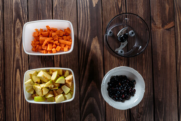 making carrot applesauce. blender bowl, blackcurrant bowl, and two white bowls of chopped vegetables and fruits