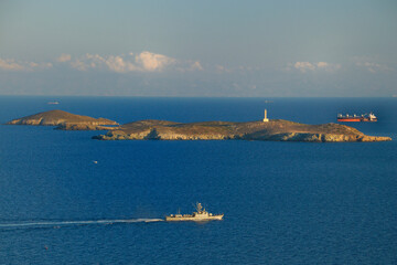 Statki pływające wokół małej greckiej wyspy z latarnią morską.
