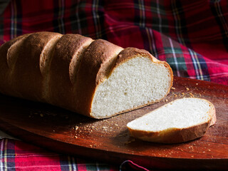 Wheat flour white bread loaf on a wooden cutting board on a red checkered tablecloth