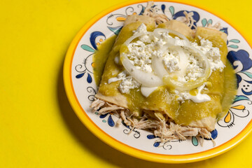 Mexican green enchiladas with chicken and cheese on yellow background
