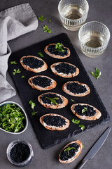 Toasts with black caviar and two glasses of white wine on grey stone background