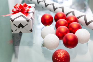 Naklejka premium Red and white Christmas balls are scattered on the glass table. Christmas gift, wrapping paper, red bow. New Year, xmas.