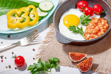Fried egg in cast iron serving pan, cherry tomatoes, beans and vegetables
