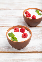 Yogurt with raspberry in clay cups on white wooden background. Side view.