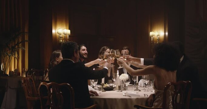 Group of men and women celebrating with wine at dinner party. Friends enjoying dinner at a gala night.
