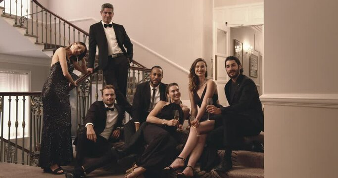 Multi-ethnic group of friends sitting at stairs and looking at camera. Group of men and woman at gala night.
