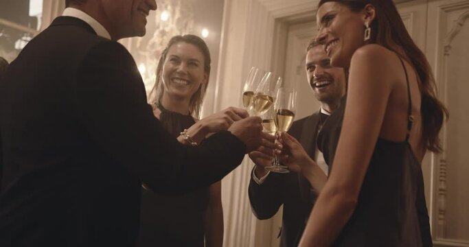 Group of people at a celebration event drinking wine. Men and women in formalwear toasting and drinking champagne at party.
