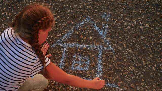 child kid draw a house on the asphalt with chalk . childhood mortgage dream kid concept. little girl playing draws with chalk big house. concept loan mortgage for a dream home residential building