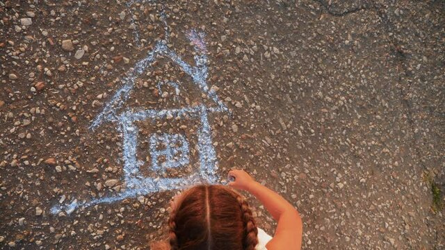 child kid draw a house on the asphalt with chalk . childhood mortgage dream kid concept. little girl playing draws with chalk home big house. concept loan mortgage for a dream residential building