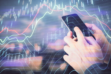 Double exposure of man's hands holding and using a digital device and forex graph drawing. Financial market concept.