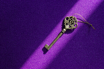 Old vintage key illuminated by ray of light on purple glitter background. Concept of hints for...