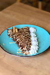 a beautifully decorated caloric pancake full of chocolate.
pancake on a red plate with lots of whipped cream.