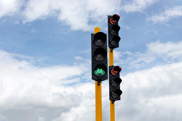 Close up to a bicycle traffic light, lighting green in a crossroad near to a traffic light lightinig red with blue sky at background