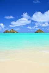 Tropical beach with turquoise waters, blue sky and view of Mokuluas at Lanikai on Oahu, Hawaii. 