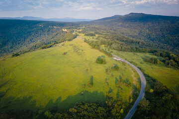 Fototapeta premium Early morning in the mountains. Morning sun and haze in the valley against the background of mountains. Green fields and meadows. The road leaving into the distance. Adygea, Russia
