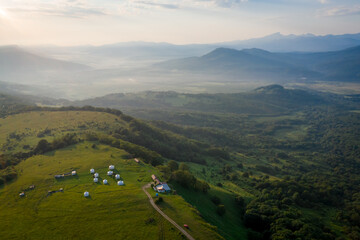 Fototapeta premium Early morning in the mountains. Morning sun and haze in the valley against the background of mountains. Mountain summer landscape. Tourist tents in the mountains