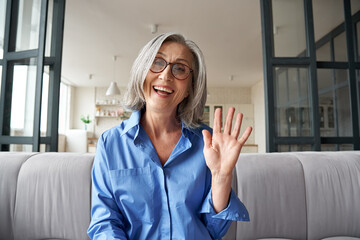 Happy mature middle aged woman online teacher waving hand talking to web cam video conference...