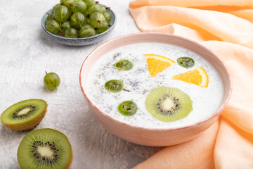Yogurt with kiwi, gooseberry, chia in ceramic bowl on gray concrete background. Side view.