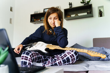 Caucasian woman sitting in her bedroom bored after having online guitar class trying to learn how to play depressed after failure - problem solving disappointment and quitting concept